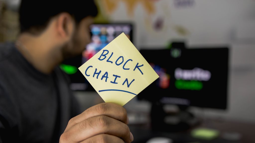 man holding paper with written blockchain