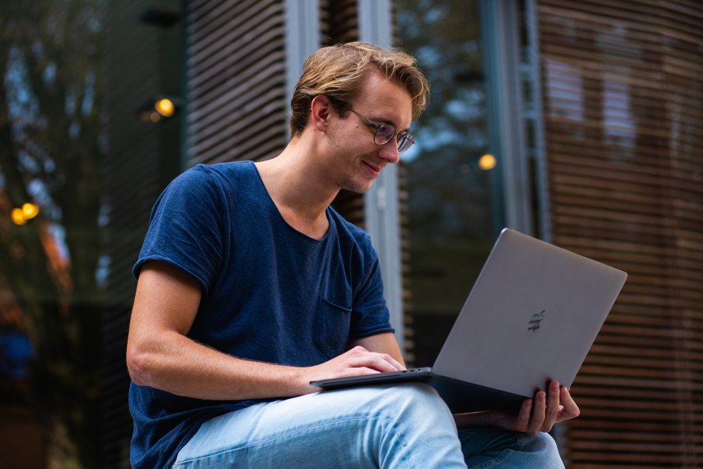 man with glasses in blue shirt using laptop